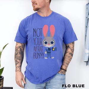 May include: A blue t-shirt with the words "NOT YOUR AVERAGE BUNNY" and a cartoon bunny character. The bunny has gray fur, pink ears, and is holding a briefcase and a flashlight. The shirt is a solid colour.
