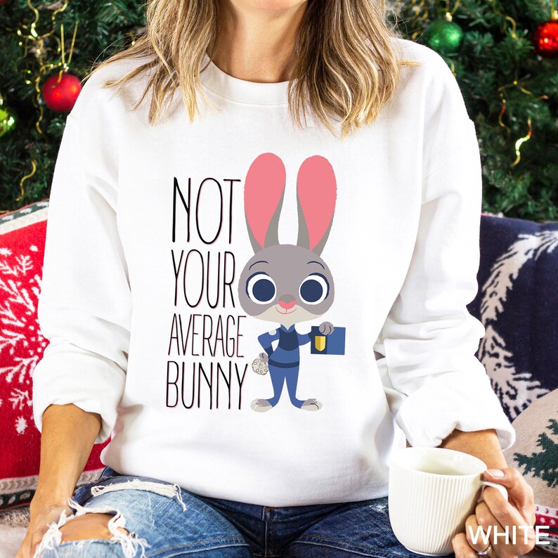 Op de afbeelding: Witte sweatshirt met een cartoon konijn in politie-uniform en de tekst "NOT YOUR AVERAGE BUNNY". Het konijn is grijs met roze oren en blauwe ogen. De sweatshirt is een crew neck stijl.