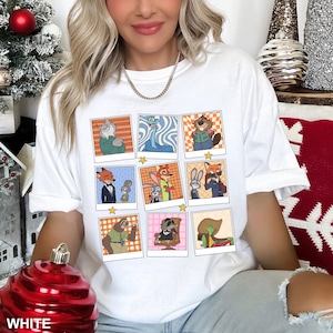 May include: White t-shirt featuring a grid of cartoon character portraits in polaroid-style frames. Each frame showcases a different character with various backgrounds. The word "WHITE" is visible at the bottom left.