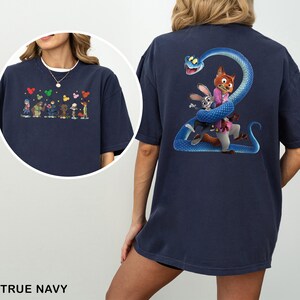 Pu&ograve; includere: T-shirt blu navy con illustrazioni di cartoni animati sul davanti e sul retro. Il davanti presenta personaggi dei cartoni animati e forme di cuore. Il retro mostra un serpente blu avvolto attorno a una volpe e un coniglio. Il testo "TRUE NAVY" &egrave; in basso.
