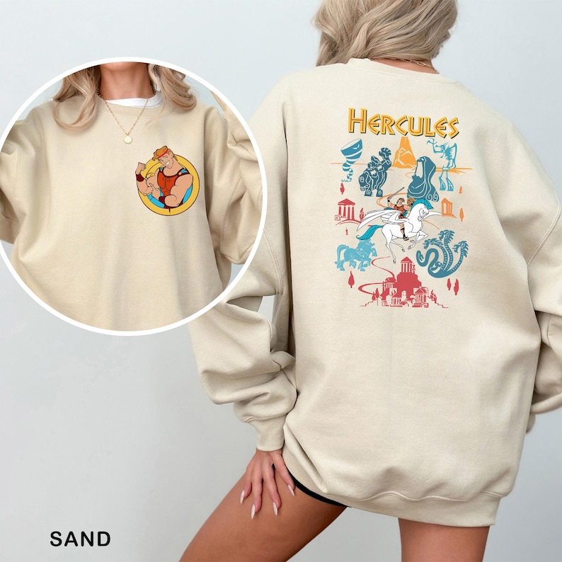 K&ouml;nnte beinhalten: Sandfarbenes Sweatshirt mit einer Cartoon-Illustration von Herkules auf der Vorderseite und einer farbenfrohen Grafik auf der R&uuml;ckseite. Die Grafik auf der R&uuml;ckseite enth&auml;lt das Wort "Hercules" in Gold sowie verschiedene Cartoon-Bilder.