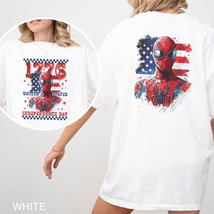 Może przedstawiać: Biały t-shirt z grafiką superbohatera Spider-Mana na tle stylizowanej amerykańskiej flagi. Projekt zawiera napis 1776, UNITED STATES oraz INDEPENDENCE DAY w kolorze czerwonym i niebieskim, z obramowaniem w szachownicę.