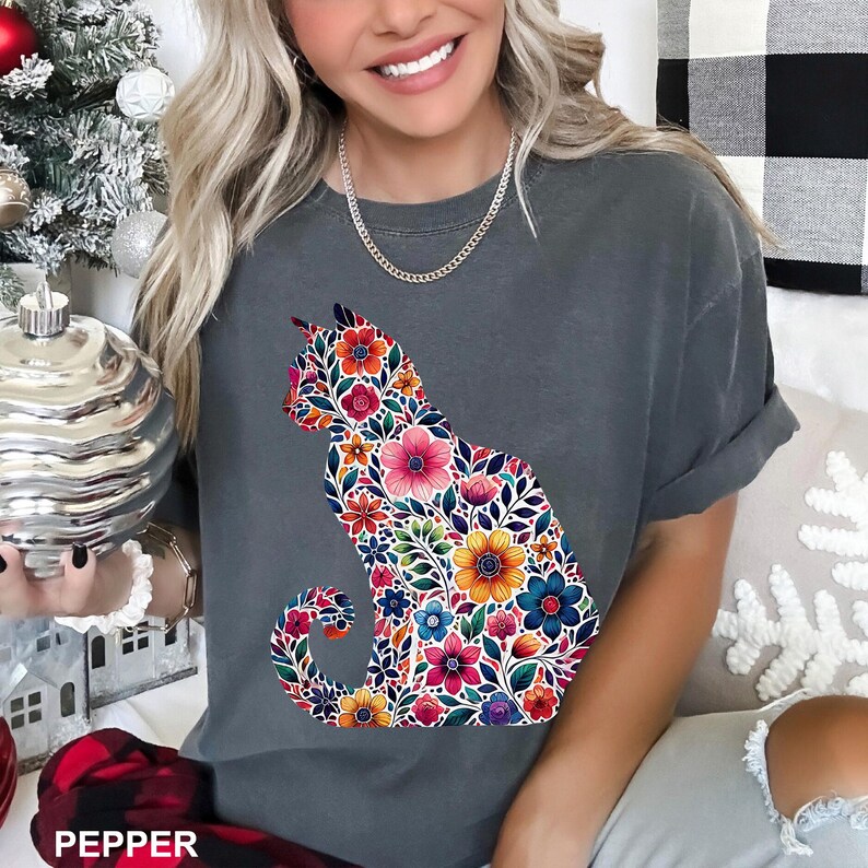 May include: A gray t-shirt featuring a floral cat design. The cat silhouette is filled with colorful flowers in shades of pink, orange, yellow, and blue. The word "PEPPER" is printed at the bottom.