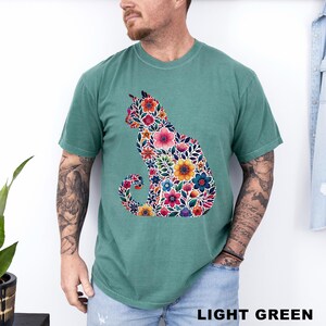 May include: Light green t-shirt featuring a floral cat design. The cat silhouette is filled with colorful flowers in shades of pink, orange, blue, and yellow. The text "LIGHT GREEN" is at the bottom of the image.