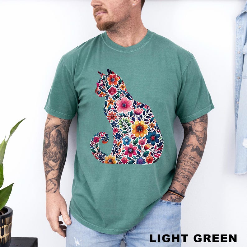May include: Light green t-shirt featuring a floral cat design. The cat silhouette is filled with colorful flowers in shades of pink, orange, blue, and yellow. The text "LIGHT GREEN" is at the bottom of the image.