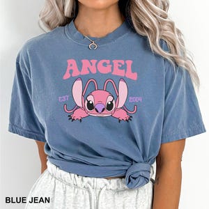 K&ouml;nnte beinhalten: Blaues Jeans-T-Shirt mit einem rosa Aufdruck der Figur Angel aus Lilo & Stitch. Das Wort "ANGEL" steht &uuml;ber der Figur, darunter "EST 2004". Das Shirt ist kurz&auml;rmlig und hat einen Rundhalsausschnitt.