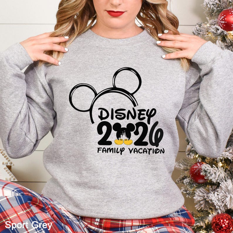 以下が含まれることがあります： 黒いミッキーマウスの頭のデザインと「DISNEY 2026 FAMILY VACATION」の文字が入った、ライトグレーのスウェットシャツ。スウェットシャツはスポーツグレーの色です。