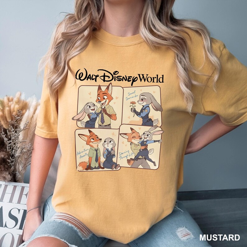 May include: Mustard-colored t-shirt featuring a Walt Disney World graphic. The graphic showcases four panels with cartoon characters, a fox and a rabbit, in various poses. Text includes "Walt Disney World", "Sweet Surrender", "Adventure Awaits", and "Dancing Through Life".