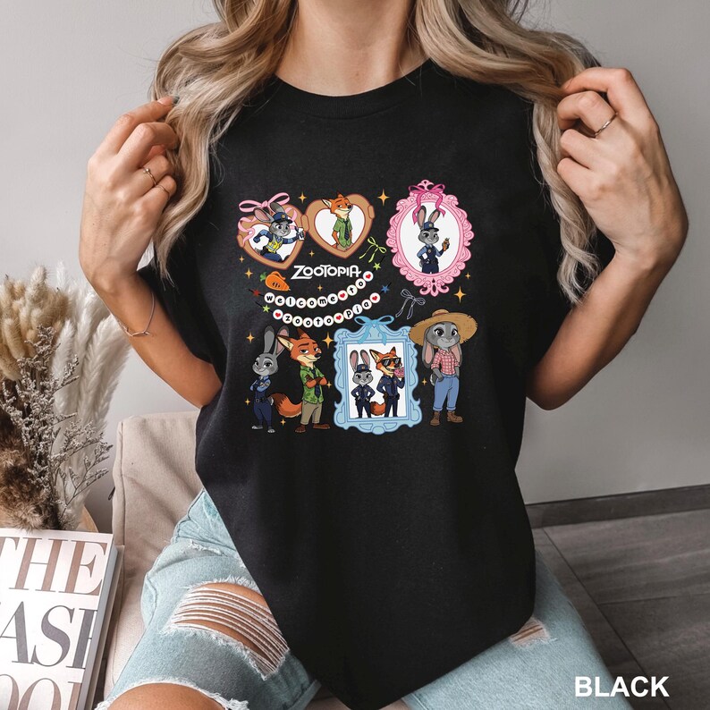 Op de afbeelding: Zwart T-shirt met ronde hals met cartoonfiguren uit de film Zootopia. Het ontwerp bevat ingelijste portretten van Judy Hopps, Nick Wilde en andere personages. Het woord "Zootopia" staat ook op het shirt.