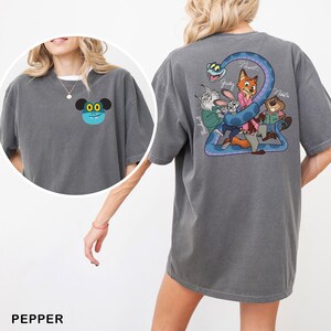 May include: Pepper-colored t-shirt featuring a cartoon character on the front and a Zootopia-themed graphic on the back. The back graphic includes Judy Hopps, Nick Wilde, and other characters. The shirt is a comfortable, oversized fit.