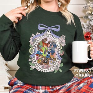 May include: Forest green sweatshirt featuring a floral oval design with cartoon characters. The design includes a purple bow and a variety of flowers. The sweatshirt is a solid forest green color.