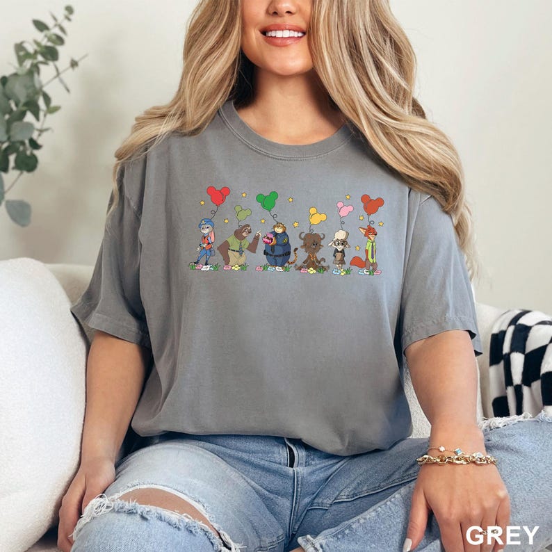 May include: A grey t-shirt featuring a colorful cartoon design of several animal characters holding heart-shaped balloons. The word "GREY" is printed in the bottom right corner. The shirt is made of a soft material.