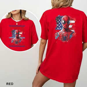 Może przedstawiać: Jaskrawoczerwony t-shirt z grafiką superbohatera Spider-Mana umieszczoną na tle stylizowanej amerykańskiej flagi. Wz&oacute;r zawiera napis UNITED STATES. Tył koszulki prezentuje większą wersję tej samej grafiki nadrukowanej na materiale.