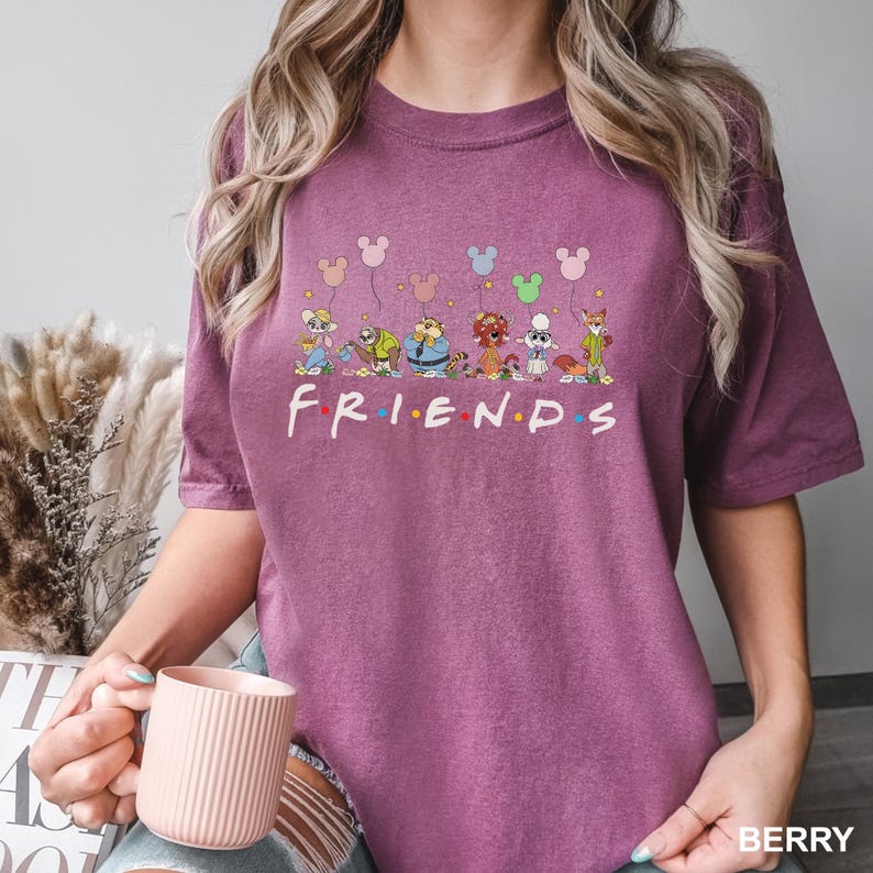 May include: Berry-colored t-shirt featuring the word "FRIENDS" in white, with cartoon characters and Mickey Mouse balloons above. The shirt has short sleeves and a crew neck.