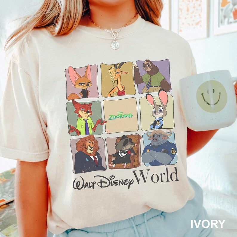 May include: Ivory-colored t-shirt featuring a grid of Zootopia characters and the text "Walt Disney World." The shirt includes images of Nick Wilde, Judy Hopps, and other characters from the animated film. A white mug with a smiley face is held in the image.