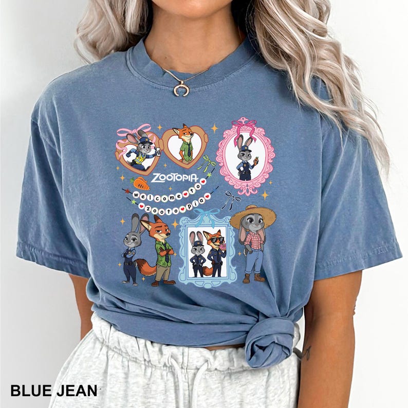Op de afbeelding: Blauw spijkerbroekkleurig T-shirt met een kleurrijke afbeelding van personages uit de animatiefilm Zootopia. Het ontwerp bevat ingelijste portretten van de personages, harten en de titel van de film. Het shirt is een comfortabele, casual stijl.