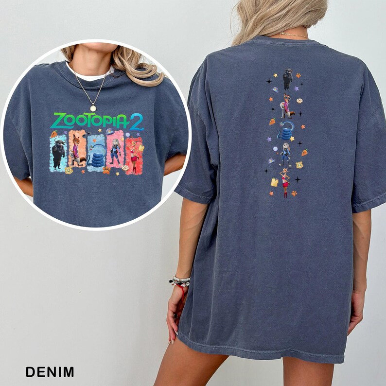 May include: Denim blue t-shirt featuring the text "ZOOTOPIA 2" with colorful character graphics on the front. The back of the shirt has a vertical design with more character illustrations and stars. A casual, oversized fit.