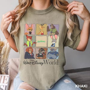 May include: Khaki-colored t-shirt featuring a grid of Zootopia characters. The shirt includes the text "Zootopia" and "Walt Disney World" in a stylized font. The shirt is a casual style.