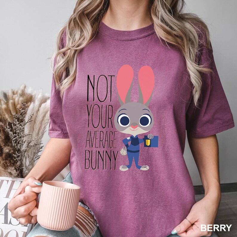 May include: Berry-coloured t-shirt with a cartoon bunny character from Zootopia. The bunny is in a police uniform and holding a briefcase. The text "NOT YOUR AVERAGE BUNNY" is printed above the character.