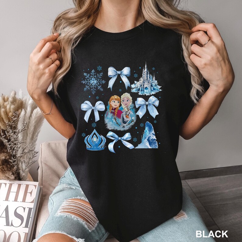 May include: Black t-shirt featuring a colorful graphic of characters from a popular animated movie, surrounded by blue bows, snowflakes, and a castle. The word "BLACK" is printed at the bottom right corner of the shirt.