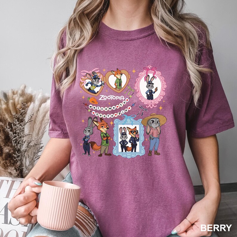 Op de afbeelding: Bessenkleurig T-shirt met meerdere ingelijste illustraties van personages uit de animatiefilm "Zootopia". Het ontwerp bevat Judy Hopps, Nick Wilde en andere personages in verschillende poses. Het woord "Zootopia" wordt ook weergegeven.
