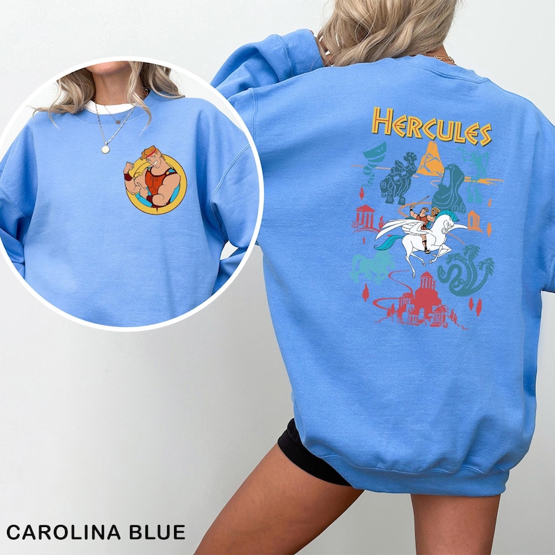 K&ouml;nnte beinhalten: Carolina-blaues Sweatshirt mit einer Cartoon-Grafik von Herkules auf der Vorder- und R&uuml;ckseite. Die vordere Grafik ist ein kreisf&ouml;rmiges Bild von Herkules, der seine Muskeln anspannt. Die hintere Grafik hat das Wort "Hercules" in Gelb, mit anderen Cartoon-Bildern.