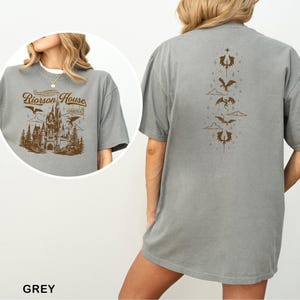 May include: Grey t-shirt with a brown graphic on the front featuring a castle, trees, and the text "Riorosn House". The back of the shirt has a vertical design of dragons and clouds. The word "GREY" is at the bottom.