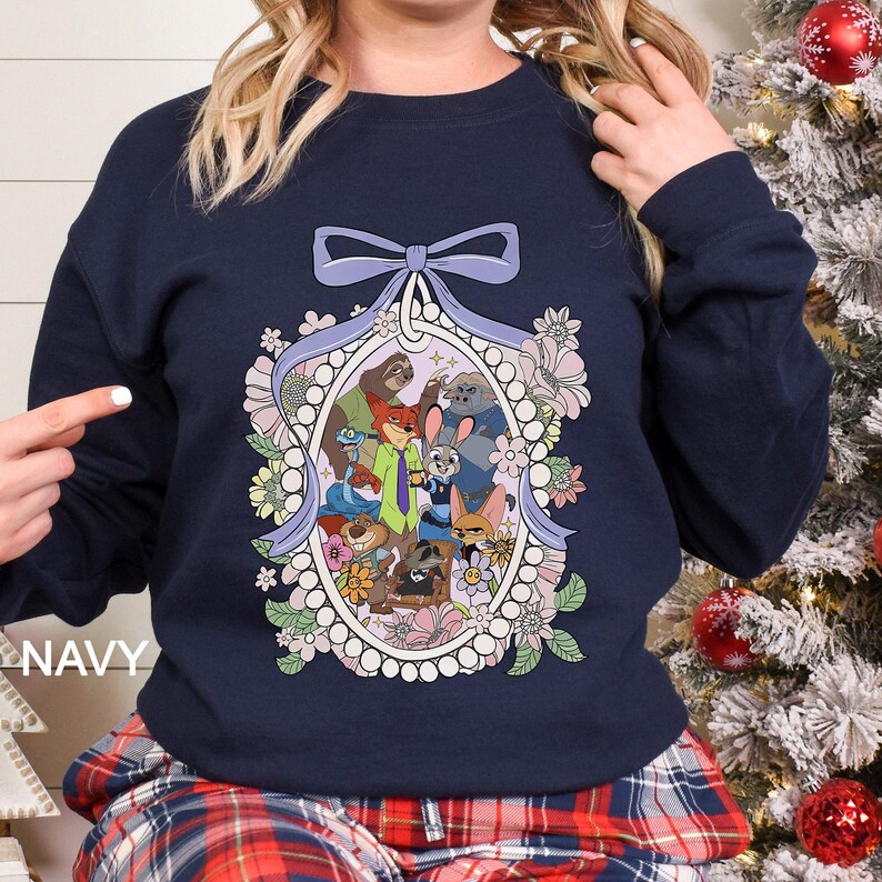 May include: Navy blue sweatshirt featuring a framed illustration of cartoon animal characters. The oval frame is surrounded by flowers and a light purple bow. The word "NAVY" is printed on the left side of the sweatshirt.