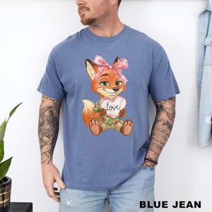 May include: Blue jean t-shirt featuring a cartoon fox with a pink bow, holding a heart-shaped sign that says "Love". The fox is wearing a Hawaiian shirt and khaki shorts. The text "BLUE JEAN" is at the bottom of the image.