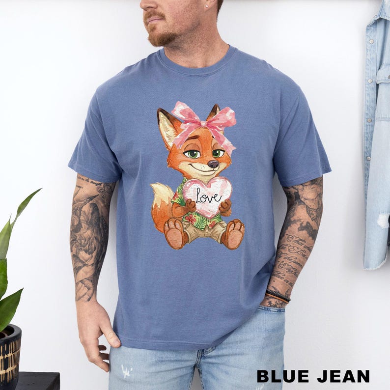 May include: Blue jean t-shirt featuring a cartoon fox with a pink bow, holding a heart-shaped sign that says "Love". The fox is wearing a Hawaiian shirt and khaki shorts. The text "BLUE JEAN" is at the bottom of the image.