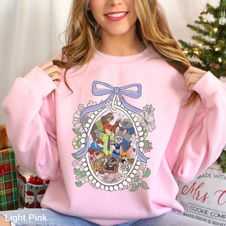 May include: Light pink sweatshirt featuring a cartoon illustration of various animal characters within an oval frame. The frame is adorned with a light blue bow and floral accents. The text "Light Pink" is visible at the bottom.
