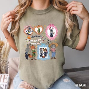 Op de afbeelding: Khaki T-shirt met een kleurrijke afbeelding van personages uit de film Zootopia. Het ontwerp bevat ingelijste portretten van de personages, het woord "Zootopia" en de zin "Welcome to Zootopia".