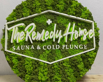 May include: A round, green moss wall sign with a white frame and the text "The Remedy House Sauna & Cold Plunge".