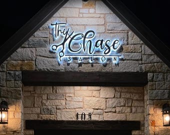 Könnte beinhalten: Ein beleuchtetes Schild für einen Salon namens "The Chase Salon" an einer Steinwand bei Nacht.
