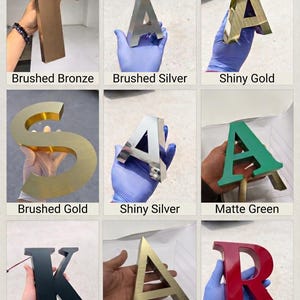 May include: A collection of nine three-dimensional letters featuring various finishes including brushed bronze, brushed silver, shiny gold, brushed gold, shiny silver, matte green, matte black, antique gold, and matte red, labeled with their respective names.