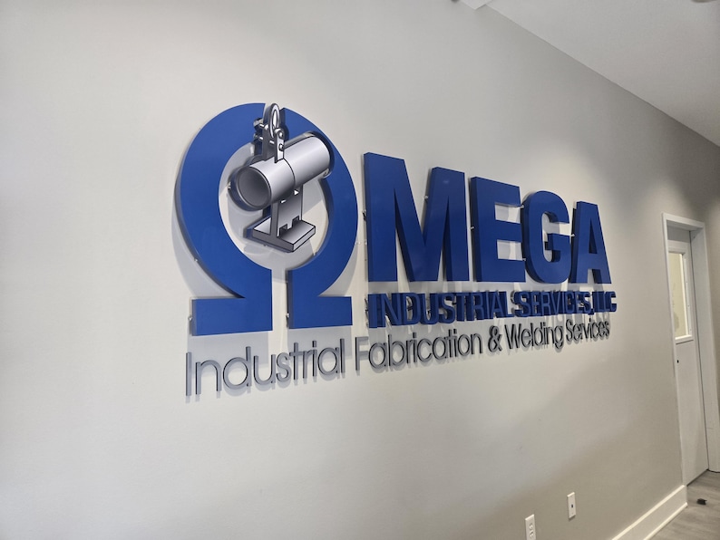 May include: A three-dimensional wall sign featuring a large blue Greek letter Omega symbol containing a silver industrial pipe icon. Next to it, the blue text reads MEGA INDUSTRIAL SERVICES, LLC, with the words Industrial Fabrication & Welding Services below.