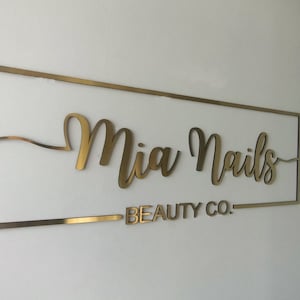 Pu&ograve; includere: Cartello in metallo dorato con il testo "Mia Nails Beauty Co." in un font corsivo.