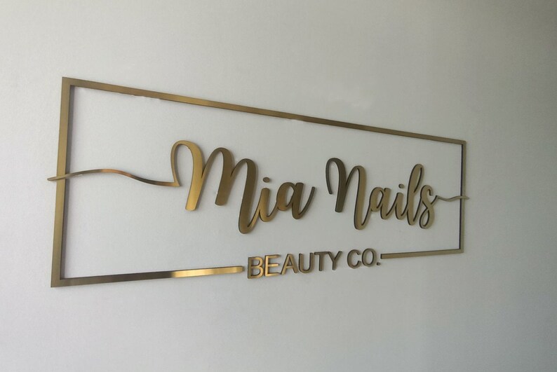 Pu&ograve; includere: Cartello in metallo dorato con il testo "Mia Nails Beauty Co." in un font corsivo.
