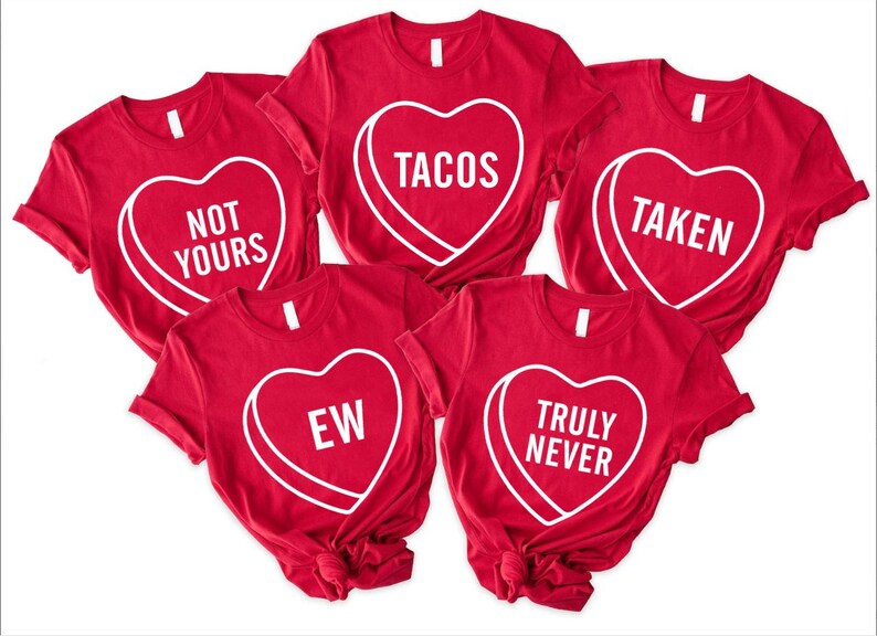 May include: Red t-shirts with white heart-shaped graphics. Each heart contains a different phrase: "NOT YOURS", "TACOS", "TAKEN", "EW", and "TRULY NEVER". The shirts are casual wear.