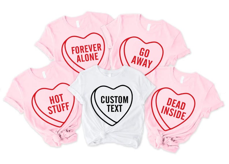 May include: A collection of pink and white t-shirts with heart-shaped designs. The pink shirts have red outlines with phrases like "Forever Alone," "Go Away," "Hot Stuff," and "Dead Inside." The white shirt features "Custom Text."