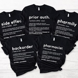 May include: Four black t-shirts with white text defining pharmacy-related terms. The shirts feature the words "side effect", "prior auth", "pharmily", "backorder", and "pharmacist".