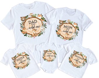May include: Set of five white t-shirts with woodland animal graphics and text that reads "Dad of the wild one", "Mom of the wild one", "Sister of the wild one", "Brother of the wild one", and "I'm the wild one".