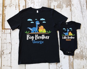 May include: Two black t-shirts with a dinosaur graphic and the text "Big Brother George" and "Little Brother Daniel".