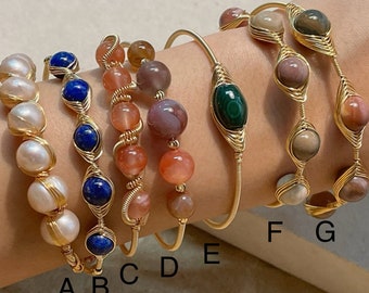 May include: Six gold wire wrapped bracelets with different gemstone beads. The bracelets are labeled A through G. The bracelets feature white pearls, blue lapis lazuli, pink and brown agate, and green malachite.