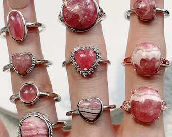May include: A hand model wearing a variety of rings with pink and white gemstone settings. The rings are all silver and feature different shapes and sizes of gemstones.