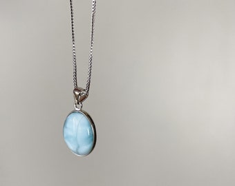 Puede incluir: Un collar de cadena de plata con un colgante ovalado azul claro. El colgante está hecho de una piedra con un patrón nublado y veteado.