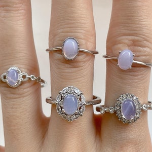 May include: Five silver rings with oval-shaped lavender gemstones. The rings are stacked on a hand, with the largest ring on the middle finger.