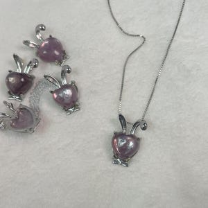 Puede incluir: Un collar de plata con un colgante de coraz&oacute;n rosa en forma de conejo. Hay cuatro dijes de conejo adicionales con corazones rosas.
