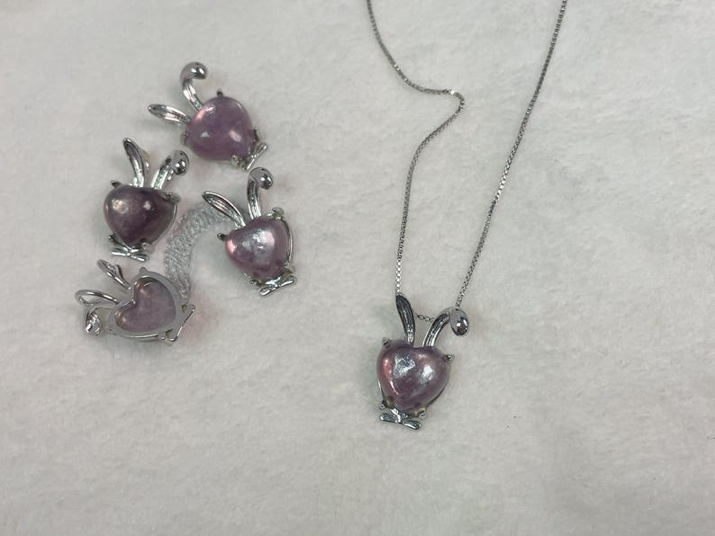 Puede incluir: Un collar de plata con un colgante de coraz&oacute;n rosa en forma de conejo. Hay cuatro dijes de conejo adicionales con corazones rosas.