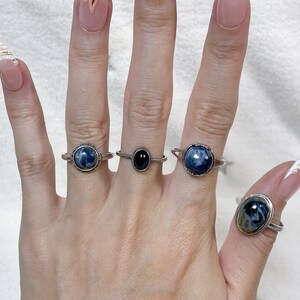 May include: Four silver-toned rings worn on fingers. Three rings feature round or oval cabochon stones with blue and black marbled patterns. One ring in the center features a smaller, smooth, solid black oval stone set in a thin band.
